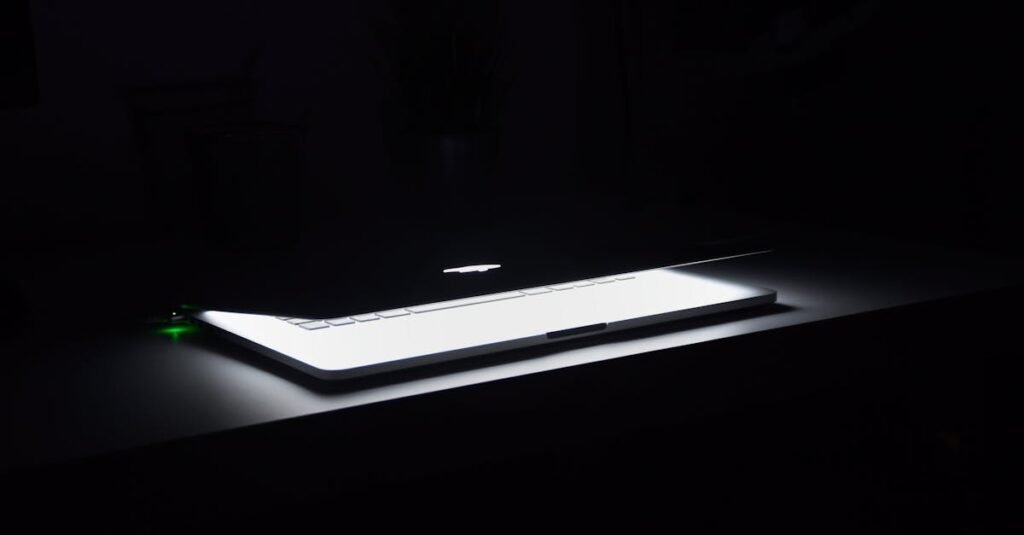 A dramatic, low-light image of a slightly open laptop with glowing keys on a dark desk.